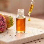 Flacon d'huile de figue de barbarie avec pipette et goutte, à côté d'une figue de barbarie coupée en deux.