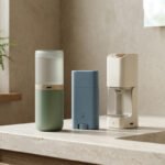 Trois produits d'hygiène 900 care zéro déchet, vert, bleu et beige, posés sur un comptoir de salle de bain. Plante en arrière-plan.