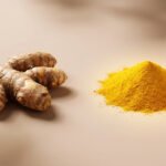 Rhizomes de curcuma frais et monticule de poudre jaune vif, éclairé, sur un fond beige uni. Illustre l'épice sous deux formes.