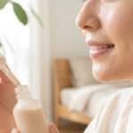 Femme souriante appliquant le Clarins BB Skin Detox avec une pipette. Son teint est lumineux et la peau saine, dans un cadre clair.