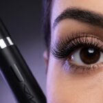 Gros plan sur un œil de femme aux cils noirs très volumineux avec un tube de mascara YSL Lash Clash noir.